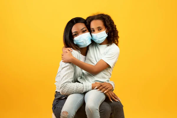 Retrato de madre e hija afroamericana con máscaras médicas protectoras en la cara sobre fondo amarillo —  Fotos de Stock