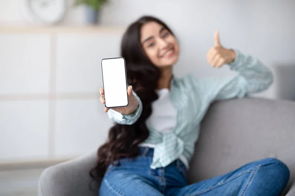 Impresionante aplicación móvil. Mujer india presentando teléfono inteligente con pantalla blanca en blanco y mostrando el pulgar hacia arriba en casa, maqueta — Foto de Stock