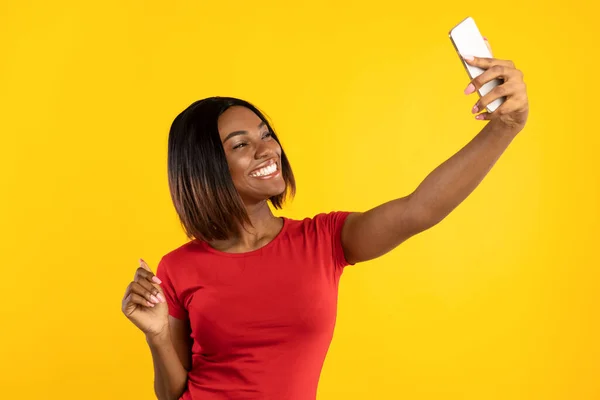 Hembra negra con teléfono inteligente haciendo selfie divertirse, fondo amarillo — Foto de Stock