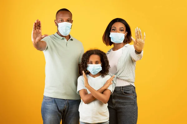 Distanciamiento social y pandemia de Covid-19. Familia afroamericana en máscaras médicas mostrando el gesto STOP fondo amarillo —  Fotos de Stock