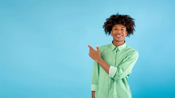 Şuraya bak. Mutlu Afrikalı Amerikalı genç adam işaret parmağıyla mavi arka plandaki boşluğu işaret ediyor. — Stok fotoğraf
