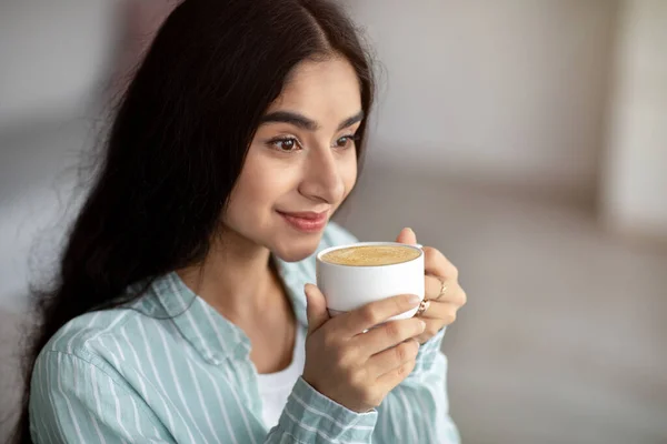 Jonge Indiase vrouw met koffiepauze, drinken schuimige cappuccino thuis, kopieerruimte — Stockfoto