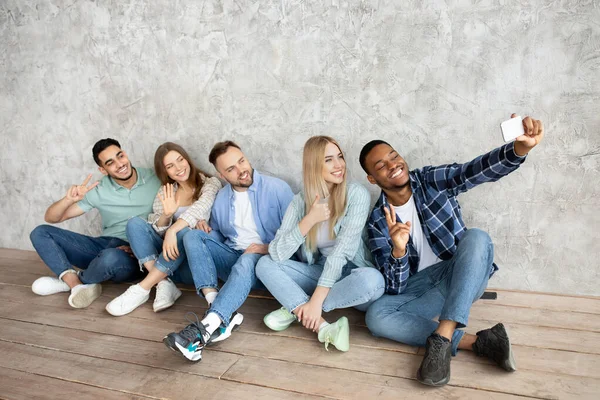 Az Y-generációs diákok teljes hossza, akik okostelefonnal szelfiznek, szürke stúdiófal mellett ülnek, másolják a helyet — Stock Fotó