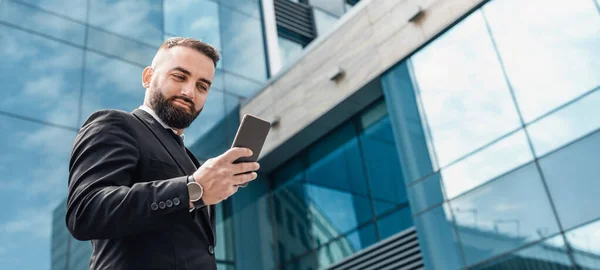 Business lifestyle concept. Confident mature businessman using smartphone, walking in urban area in city, panorama