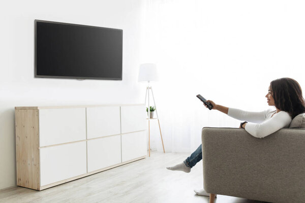 Lady watching TV holding remote control and switching channels on flatscreen plasma with blank black screen