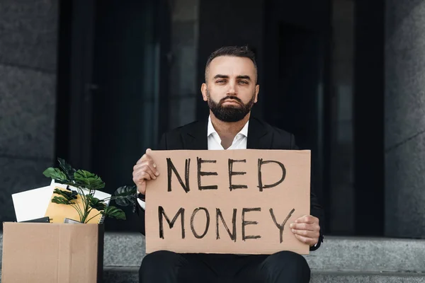 Pénzre van szükségem. Kétségbeesett, érett üzletember, kartontáblával a kezében, üzleti központ közelében a szabadban. — Stock Fotó
