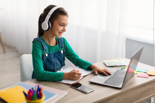 Dziewczyna siedząca przy biurku, używająca laptopa, pisząca podręcznik — Zdjęcie stockowe