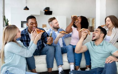 Olumlu farklı arkadaşlar evde parti veriyor, kanepede oturuyor, birayla pizza yiyor, birlikte eğleniyorlar.