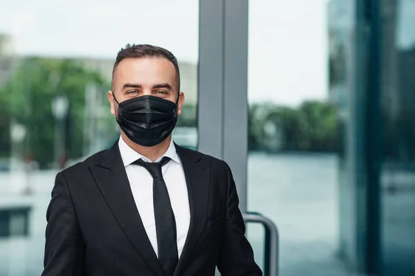 Closeup retrato de empresário maduro em preto máscara protetora médica posando ao ar livre, espaço de cópia — Fotografia de Stock