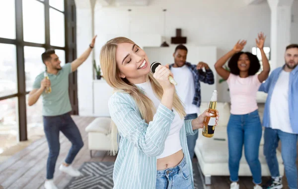 즐거운 젊은 금발의 금발 여자 가 집에서 국제 친구들 과 파티에서 노래방 노래를 부르고 있다 — 스톡 사진