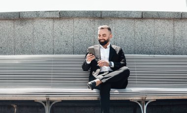 Başarılı, olgun iş adamı akıllı telefon kullanıyor, sokakta dinleniyor, bankta oturuyor ve mobil uygulama kullanıyor.