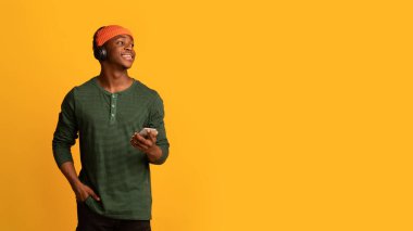 Akıllı telefonlu ve kablosuz kulaklıklı mutlu siyah hippi adam yan tarafa bakıyor.