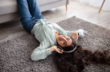 Kulaklıklı, sevimli Hintli bayanın müzik dinlediği, evdeki yumuşak halıda uzandığı manzaranın üstünde.