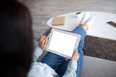 Kanepede oturan tanınmayan Hintli kadın evde boş ekranlı tablet kullanıyor. Uygulama veya web sitesi için maket yapıyor.