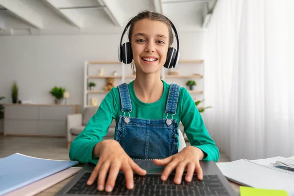 Menina sentada na mesa, usando laptop, usando fone de ouvido, digitação — Fotografia de Stock