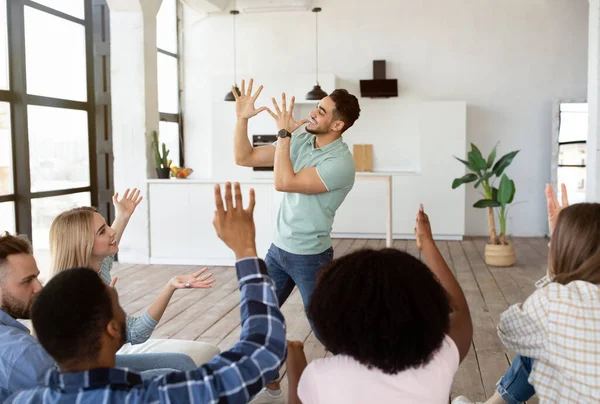 Jóvenes amigos diversos jugando charadas juego en casa. árabe chico mostrando pantomima enigmas, sus compañeros estudiantes adivinando — Foto de Stock