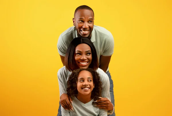 Koncepcja promocji. Happy black family of three looking side at free copy space on yellow studio background — Zdjęcie stockowe