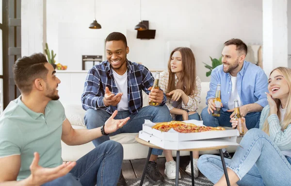 Groep internationale mannelijke en vrouwelijke vrienden die thuis pizza eten en bier drinken — Stockfoto