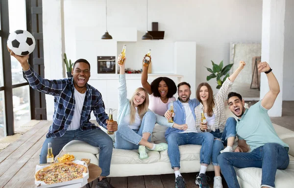 Emocjonalni międzynarodowi przyjaciele oglądają mecz piłki nożnej w telewizji, piją piwo i jedzą przekąski w domu — Zdjęcie stockowe