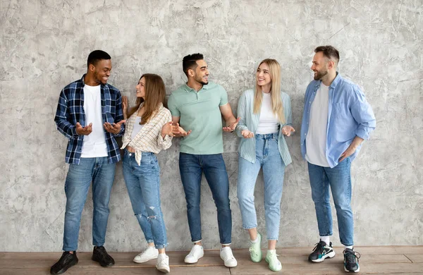 Groupe de jeunes amis divers ayant une conversation, bavardant les uns avec les autres contre le mur de studio gris, pleine longueur — Photo