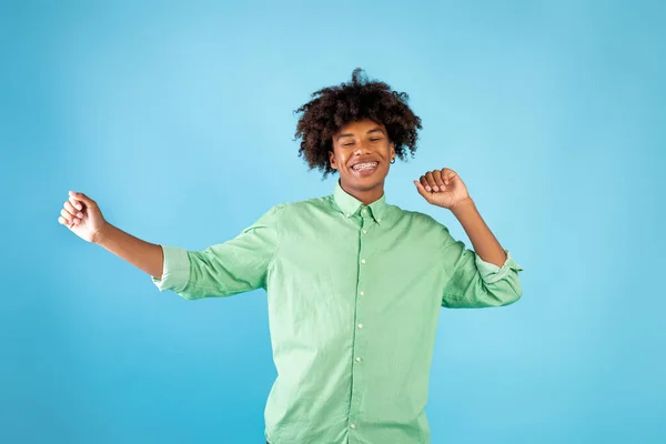 Écouter de la musique cool de la tête. Joyeux noir adolescent gars mouvement danse sur fond bleu, célébrer le succès — Photo