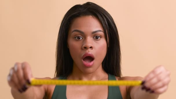 Mujer negra mostrando cinta métrica después del aumento de peso, fondo beige — Vídeos de Stock
