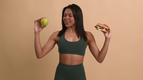 アフリカ系アメリカ人フィットネス女性バーガー対アップル、ベージュの背景を選択 — ストック動画