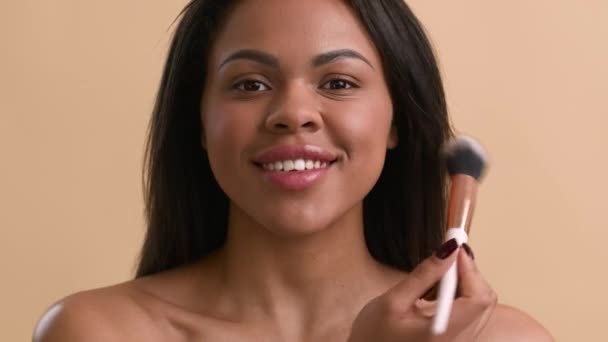 Mujer afroamericana feliz haciendo maquillaje con cepillo, fondo beige — Vídeos de Stock