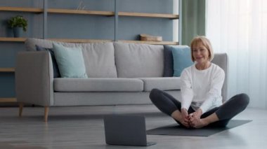 Kıdemli Fitness Kadını Laptop 'ta egzersiz yapıyor. Evde geriniyor.