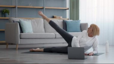 Kıdemli bayan evdeki laptopta bacak egzersizi yapıyor.