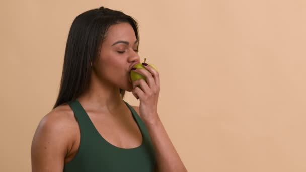 Negro aptitud señora comer manzana posando mirando al lado, beige fondo — Vídeo de stock