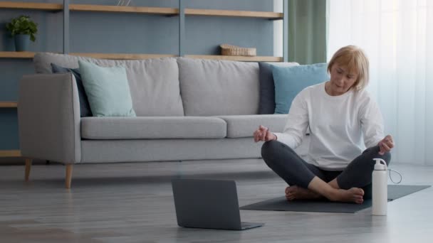 Exercício feminino sênior no laptop girando pescoço sentado em casa — Vídeo de Stock