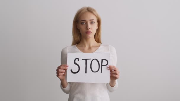 Stop vrouwelijke discriminatie. Studio portret van jonge ongelukkige vrouw poseren met poster STOP over witte muur achtergrond — Stockvideo