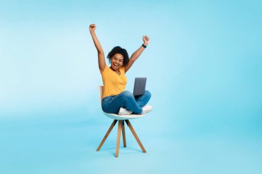 Heyecanlı genç bir kadın dizüstü bilgisayarla koltukta oturuyor, ellerini kaldırıyor, bağırıyor, kumarhane bahsini kazanıyor ya da online oyun oynuyor.