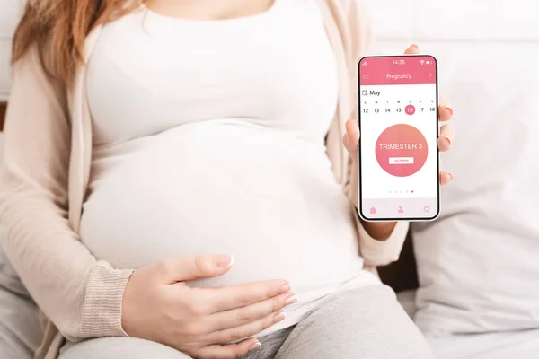 Wanita hamil tak dikenal yang menunjukkan aplikasi seluler untuk kehamilan — Stok Foto