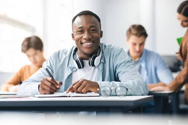 Negro macho estudiante sentado en escritorio escritura en aula — Foto de Stock