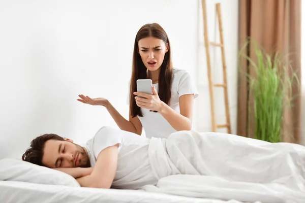 Mujer sorprendida leyendo infiel maridos mensajes en el teléfono celular en el dormitorio —  Fotos de Stock