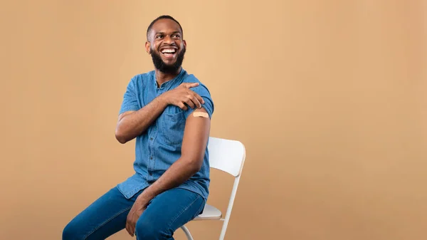 A vacinação contra o coronavírus salva a bandeira da vida. Homem negro alegre posando com ajuda de banda no braço depois de receber vacina vívida — Fotografia de Stock