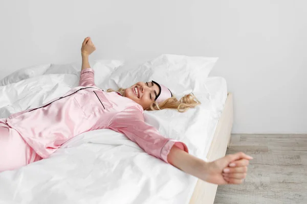Ξανθιά γυναίκα με ροζ πιτζάμες, μάσκα ύπνου ξύπνα, τεντώνεται. — Φωτογραφία Αρχείου