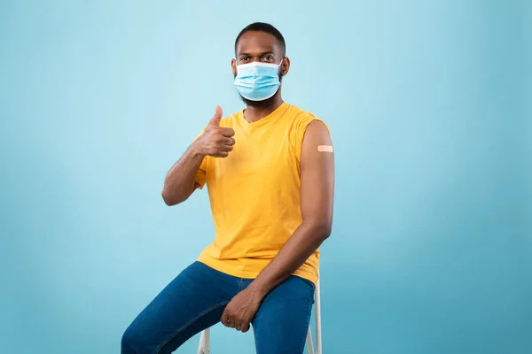 Glada vaccinerade svarta killen med självhäftande plåster bandage på armen efter coronavirus vaccin injektion visar tumme upp — Stockfoto