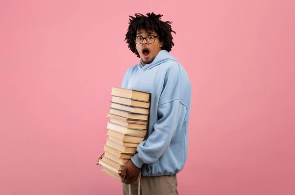 Muitos trabalhos de casa. Estudante adolescente negro aterrorizado de pé com enorme pilha de livros, abrindo a boca em choque — Fotografia de Stock