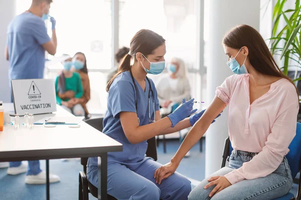 Mulher nova que recebe a injeção da vacina do Coronavirus que senta-se com o doutor interno — Fotografia de Stock