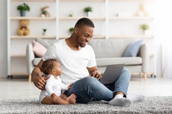 Jovem negro trabalhando no laptop e cuidando do bebê infantil — Fotografia de Stock