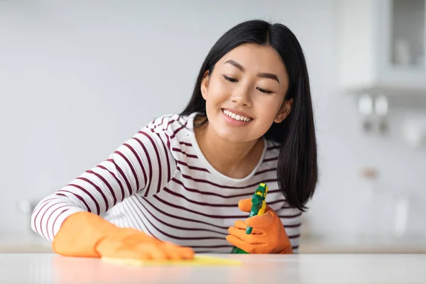 Glücklich asiatisch dame putzen küchentisch mit spray und tuch — Stockfoto