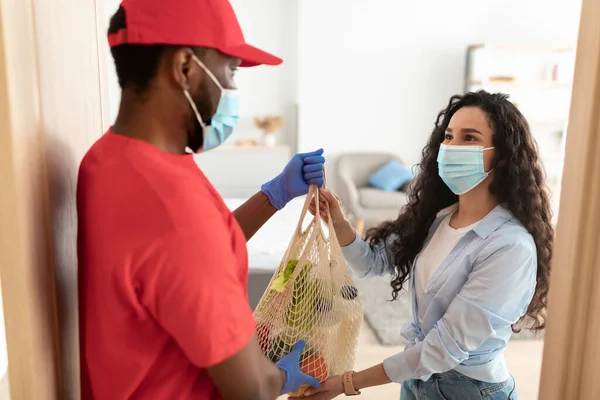 Black deliveryman in mask giving net mesh bag to woman — Stock Photo, Image