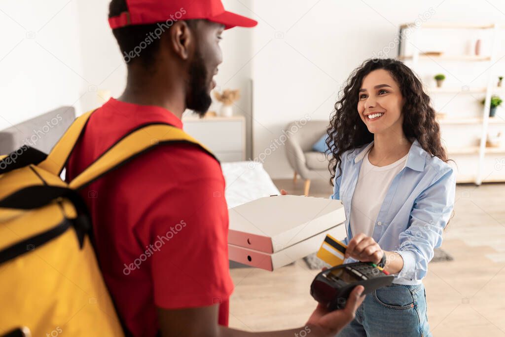 Smiling deliveryman holding POS machine, woman paying with bankcard