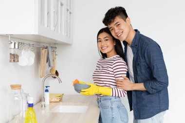 Güzel Asyalı bayan bulaşık yıkıyor, eldiven giyiyor.