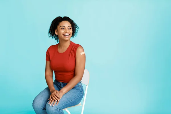 Positive schwarze Frau, die gegen Coronavirus geimpft wird, zeigt Arm mit Bandhilfe auf blauem Hintergrund, Kopierraum — Stockfoto
