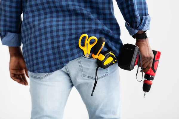 Gereedschap voor boren en fixeren. Afro-Amerikaanse man met elektrische boor, meetlint en schaar in zak — Stockfoto