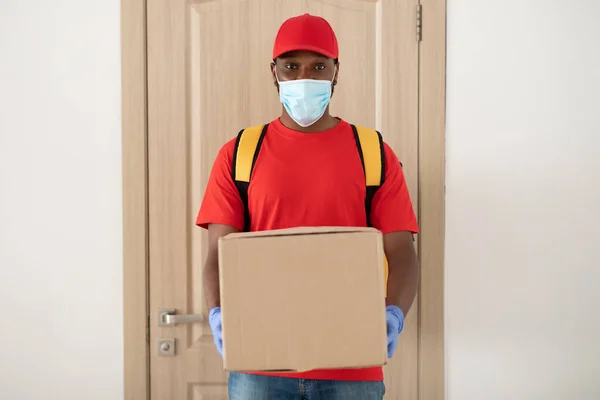 Repartidor negro en máscara médica y guantes sosteniendo paquete —  Fotos de Stock
